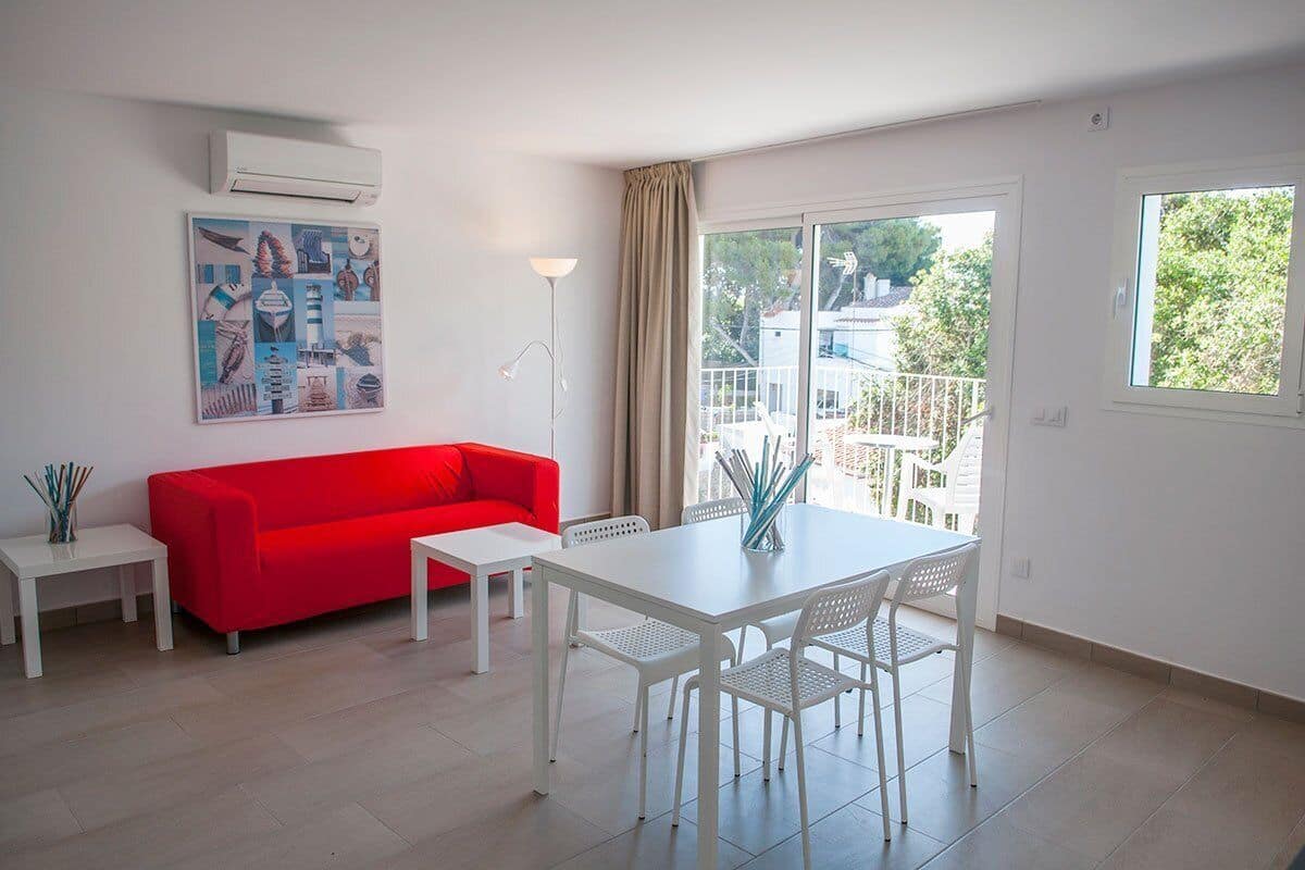 A modern living room with a red sofa, white furniture, and a balcony with a view.