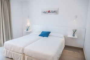 A hotel room with two beds, a blue pillow, and wall-mounted shelves with decorative items. - Petit Xuroy (Sant Lluis)