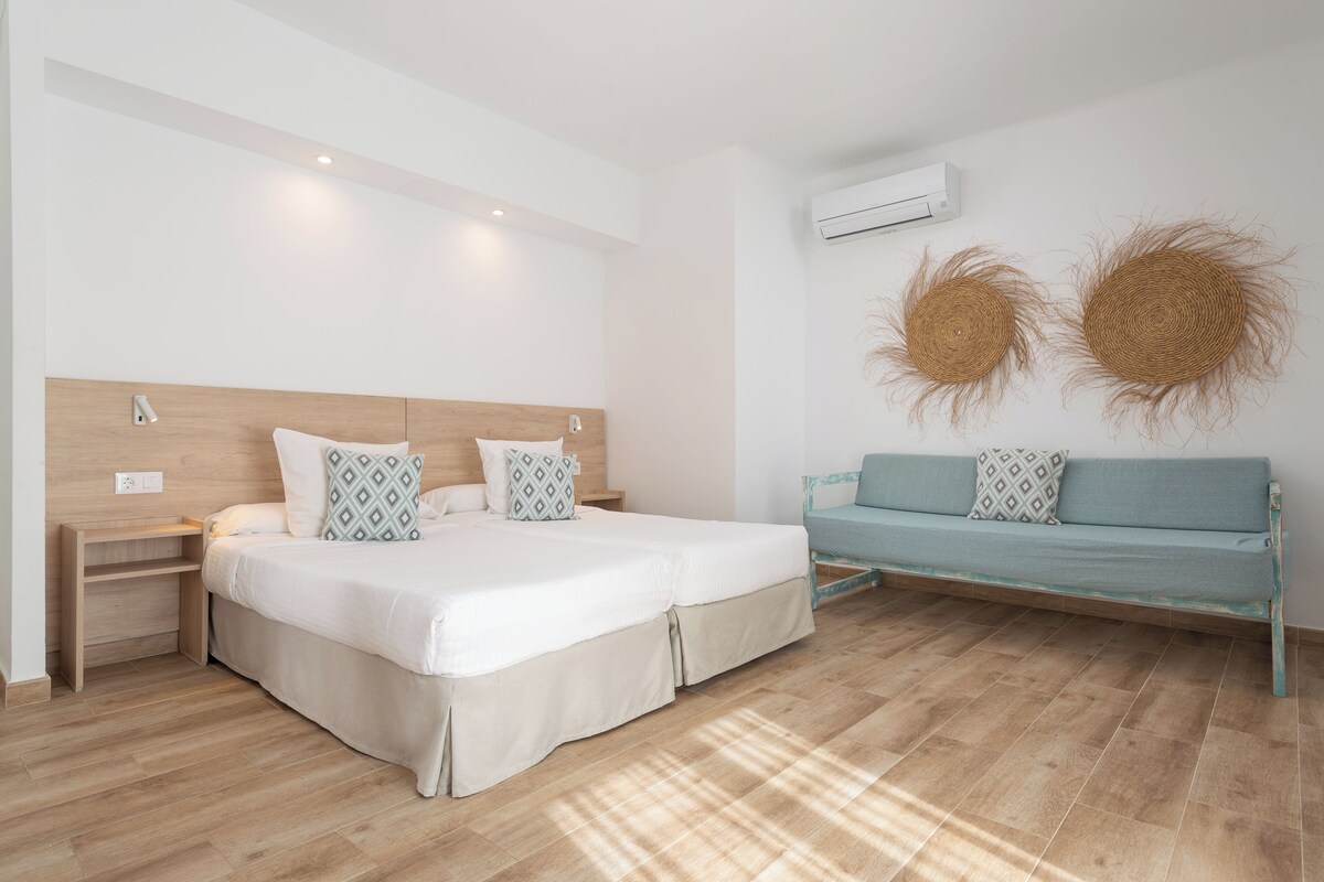 Un dormitorio con cama doble, mesitas de noche, un sofá y dos adornos en las paredes.