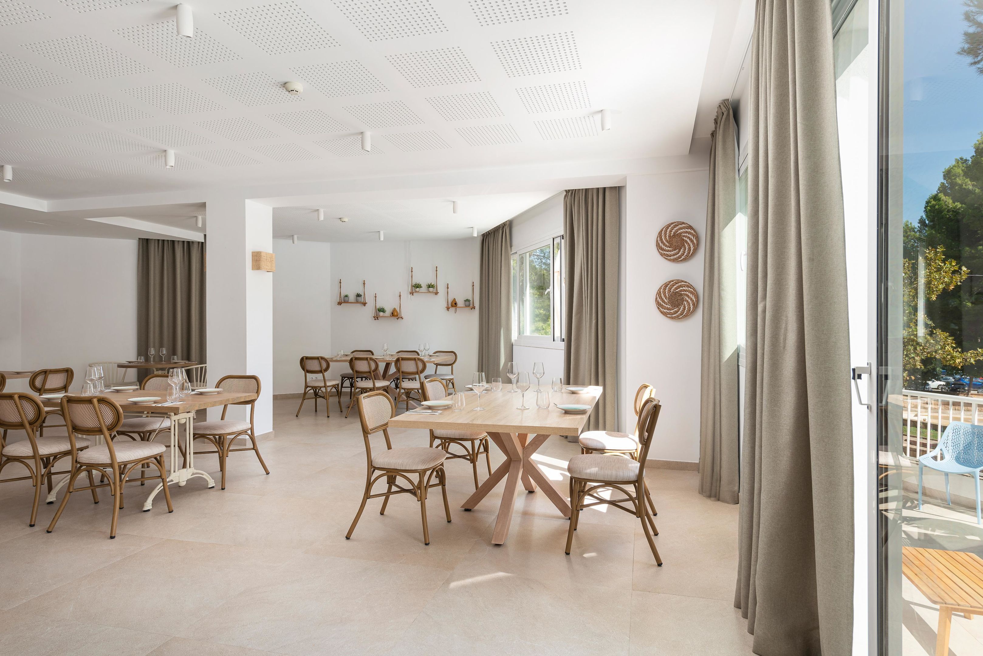 A spacious dining area with a large wooden table and wicker chairs, surrounded by large windows with curtains.