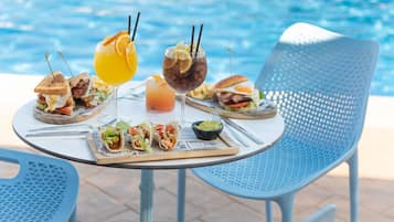Une table à manger, dressée avec divers plats et boissons, se trouve près d’une piscine.