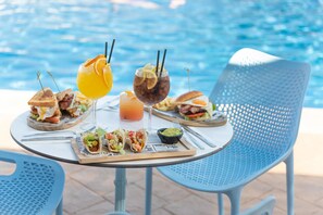 Une table à manger, dressée avec divers plats et boissons, se trouve près d’une piscine.