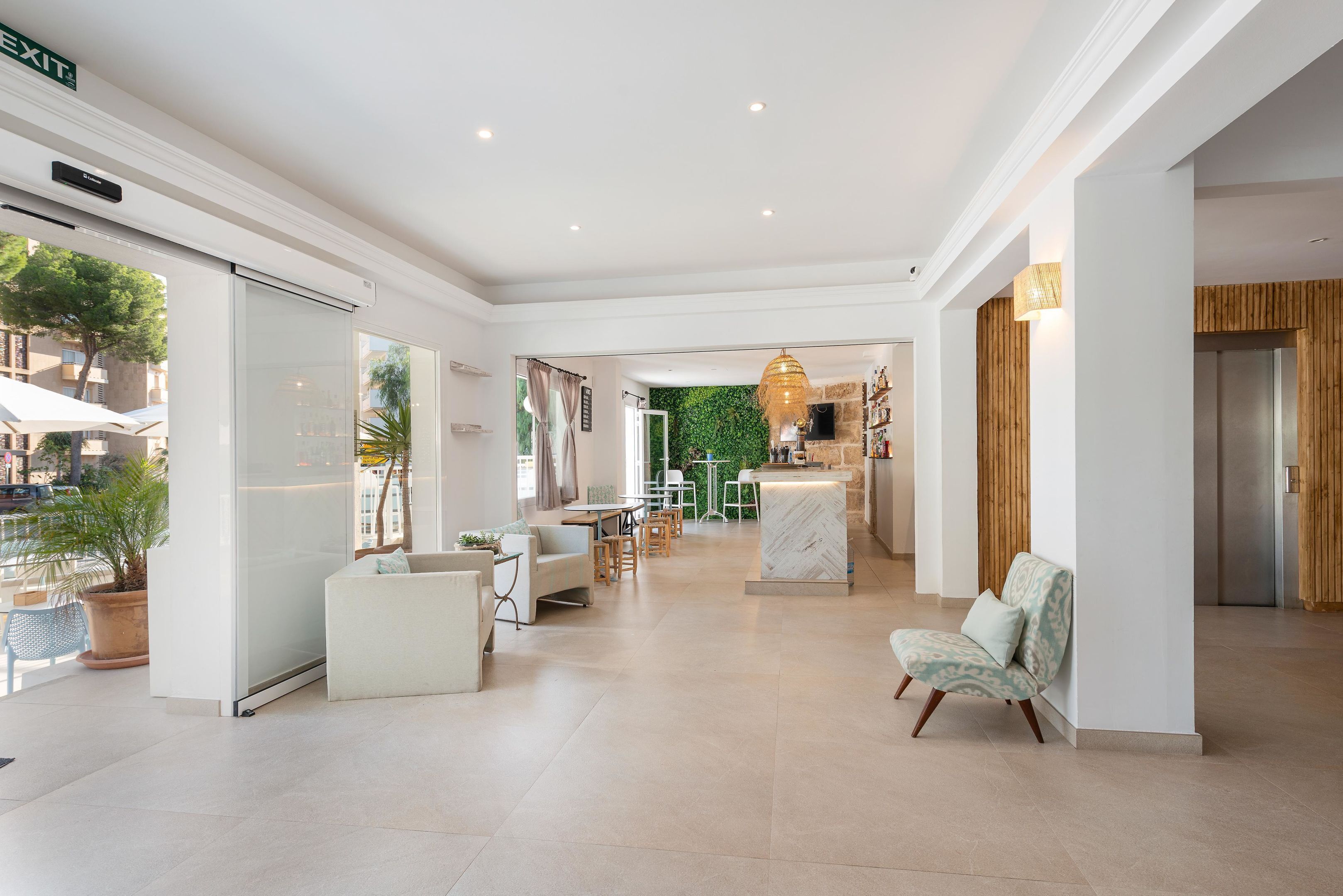 A spacious hotel lobby with a modern design, featuring a seating area, a reception desk, and a view of the outdoor area.