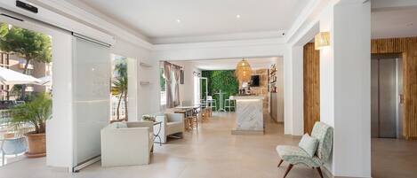 A spacious hotel lobby with a modern design, featuring a seating area, a reception desk, and a view of the outdoor area.