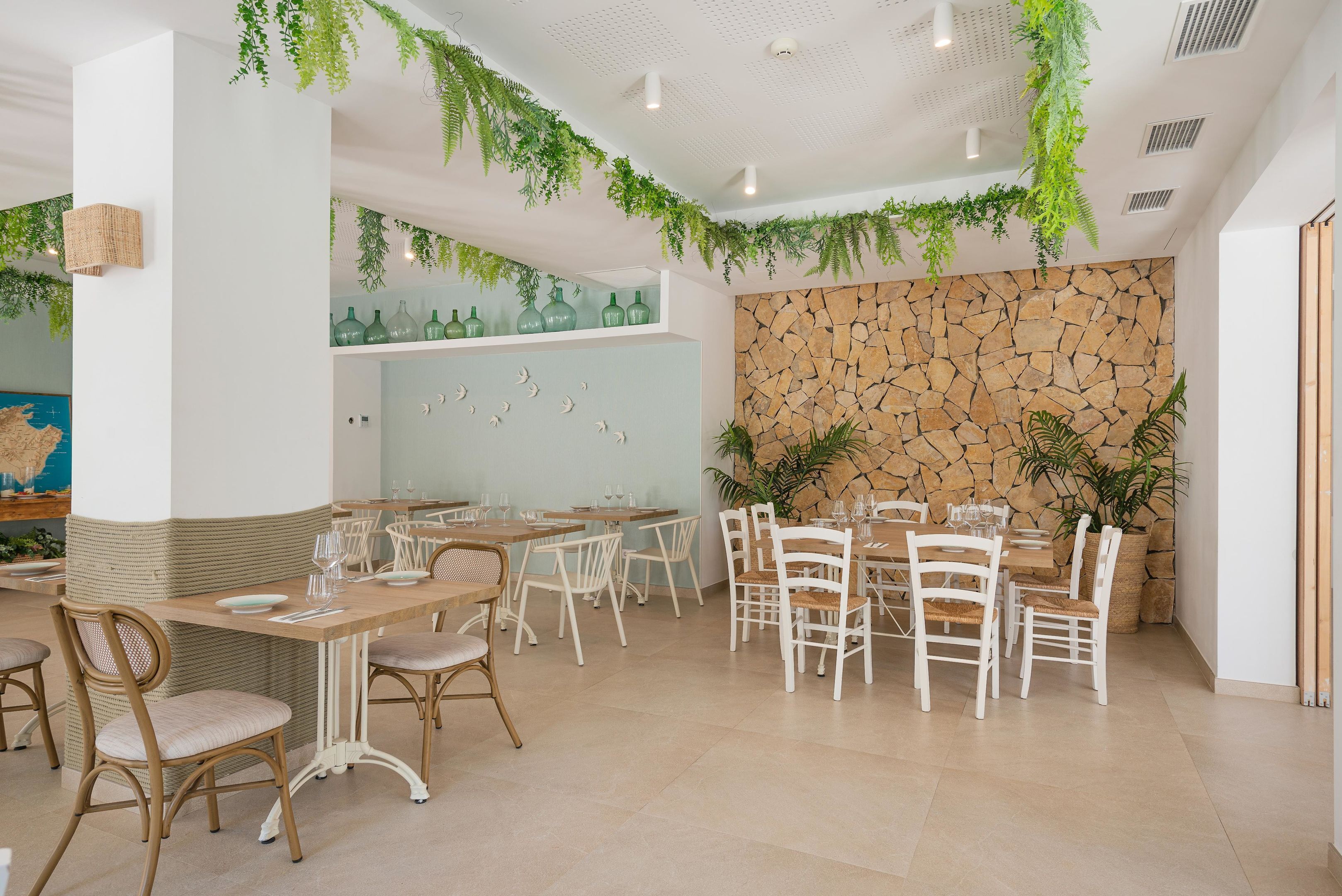 A restaurant with multiple tables and chairs, a stone wall, and hanging plants.