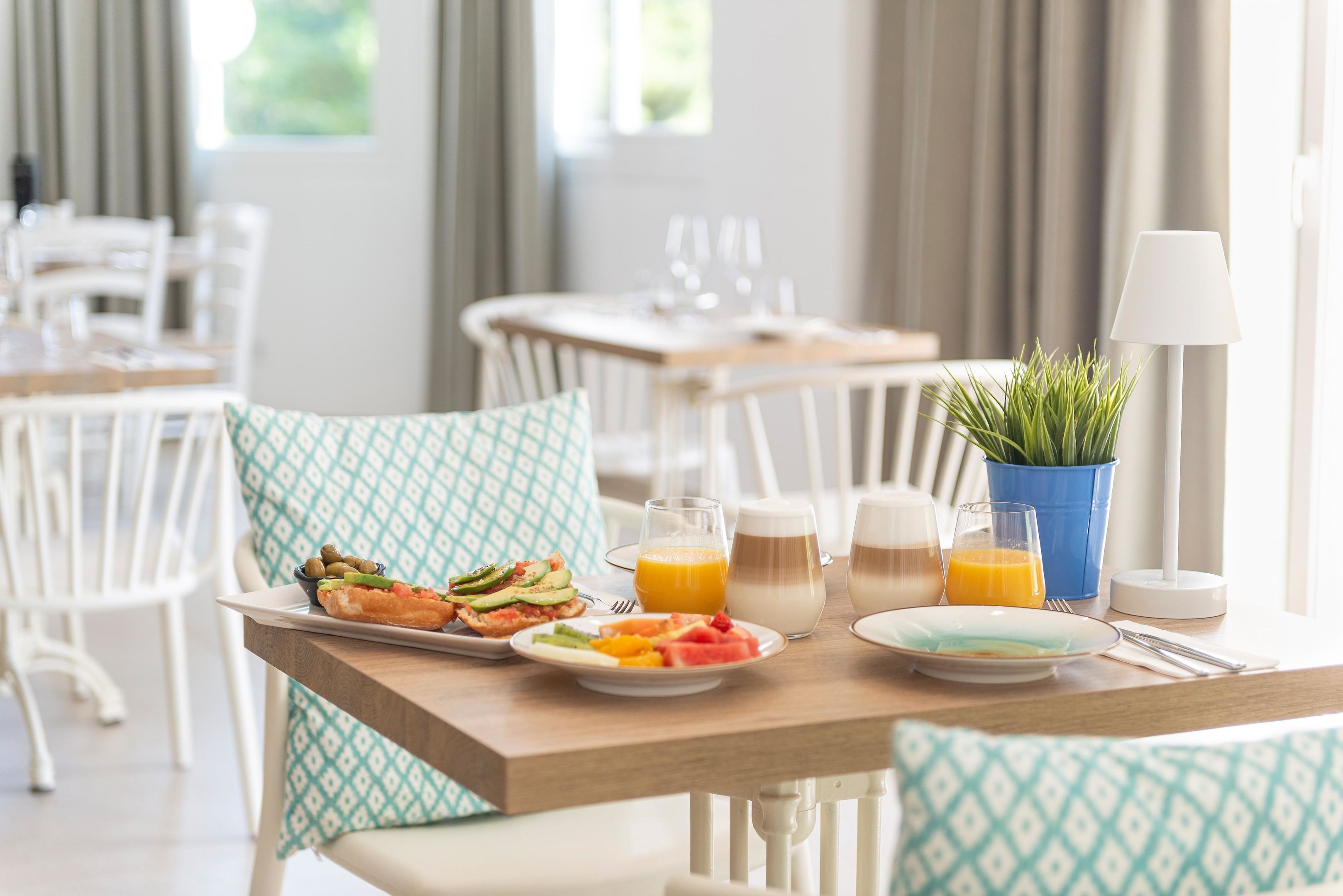 Une table de petit-déjeuner avec des assiettes remplies de nourriture, des verres de jus d’orange et une lampe.