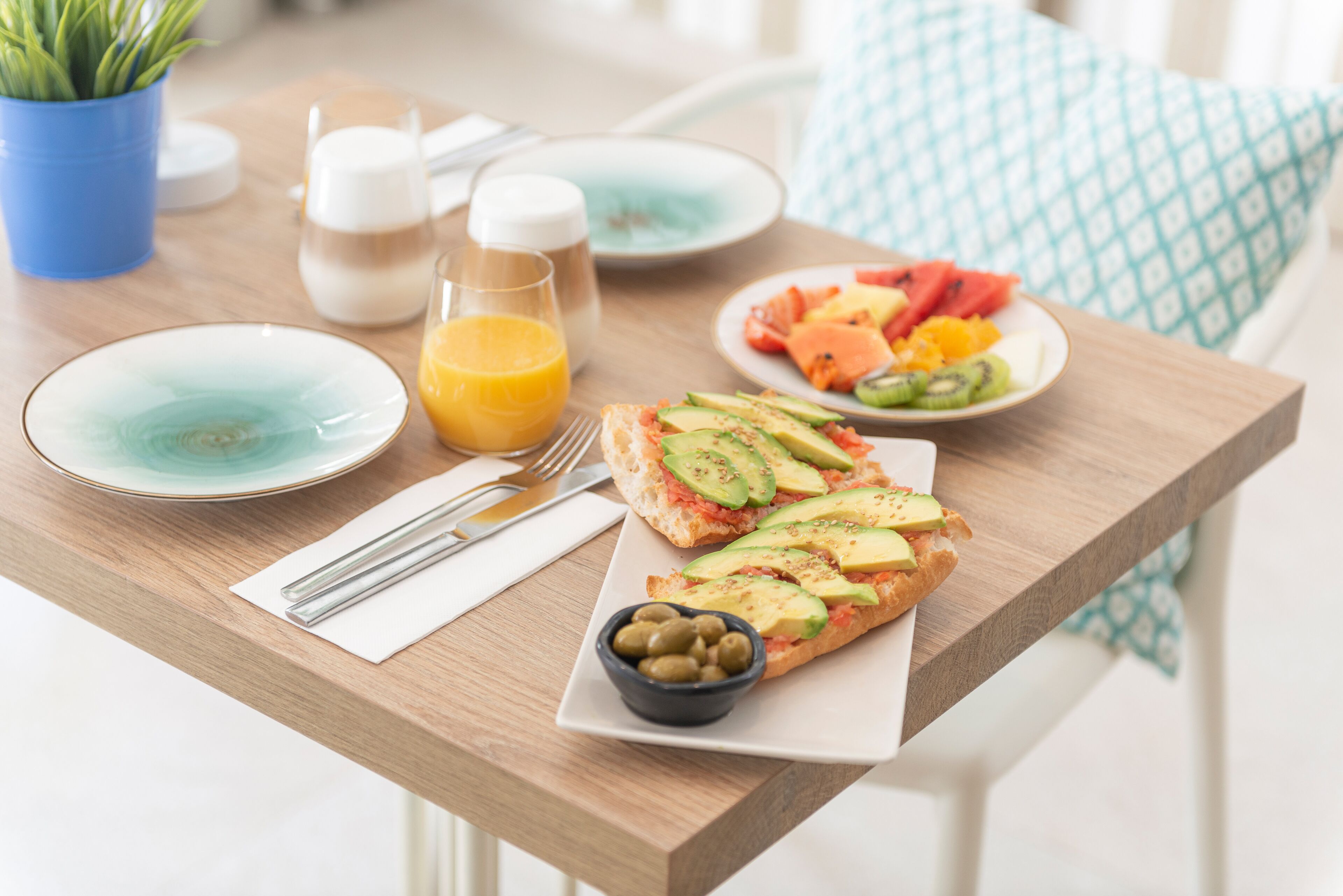 A breakfast table with plates of food, a glass of orange juice, and a bowl of olives.