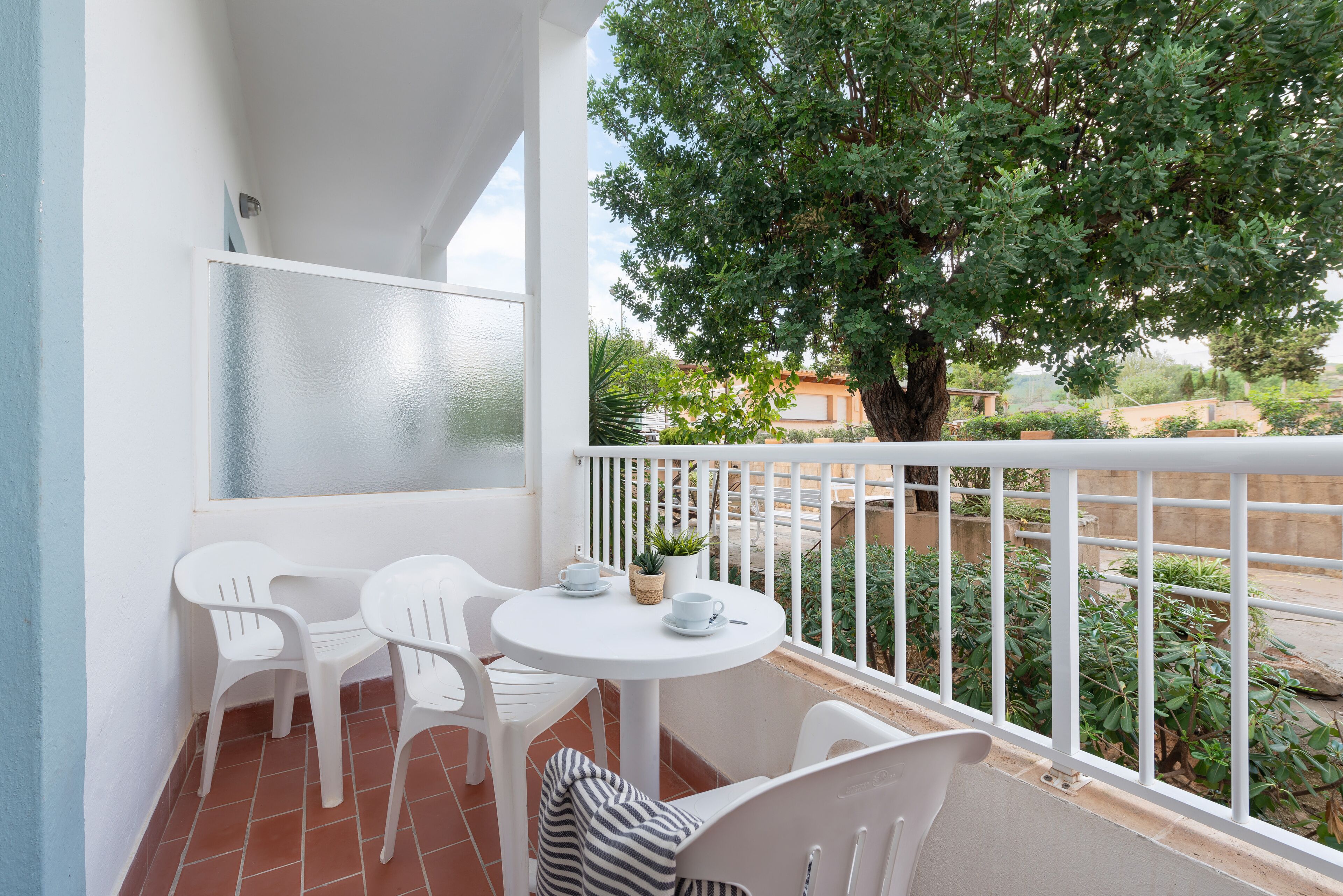 A balcony with white chairs, a small table, and a potted plant.