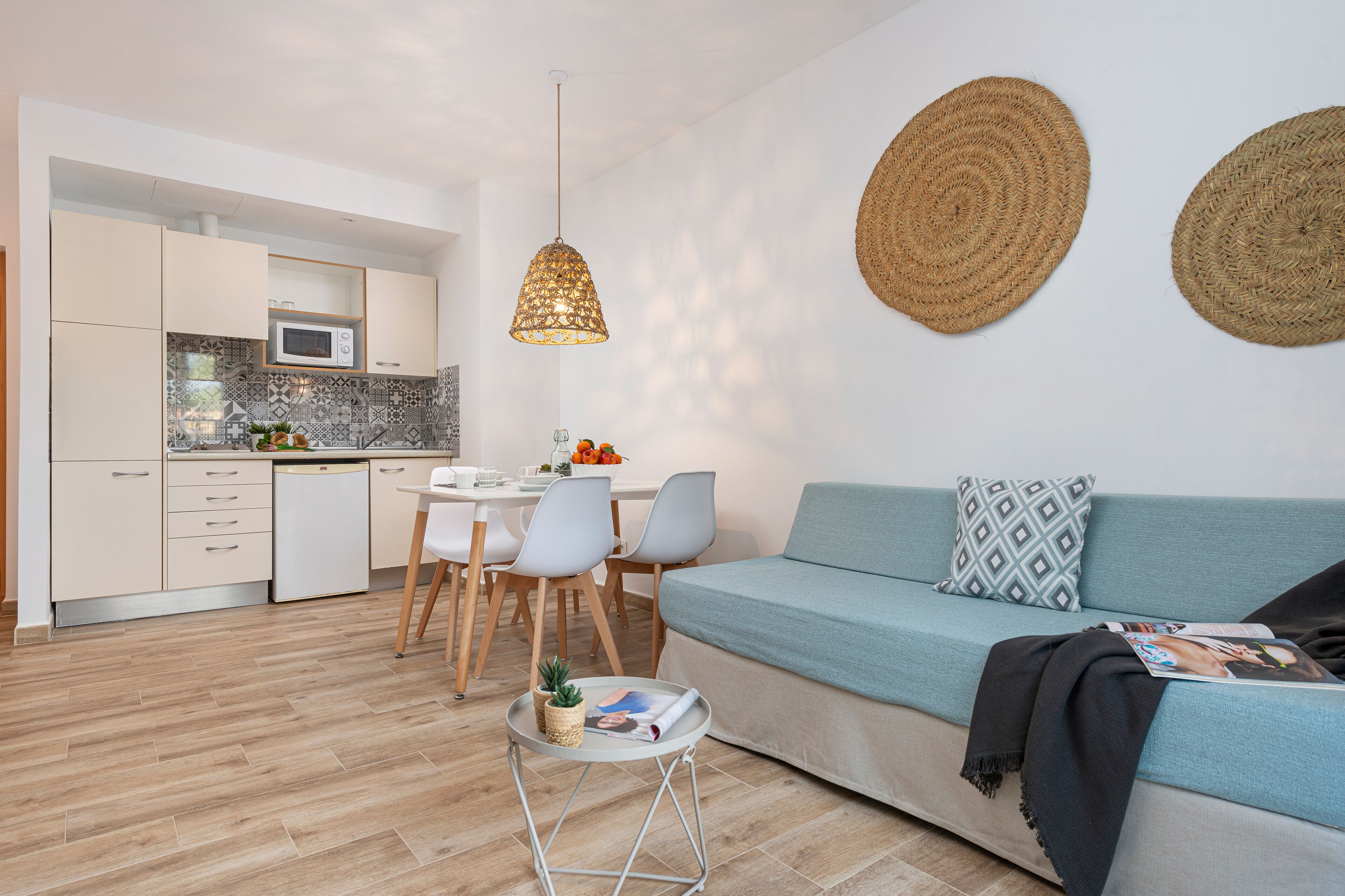 A modern kitchen with white cabinets, a dining area with a table and chairs, and a living area with a sofa and a magazine.