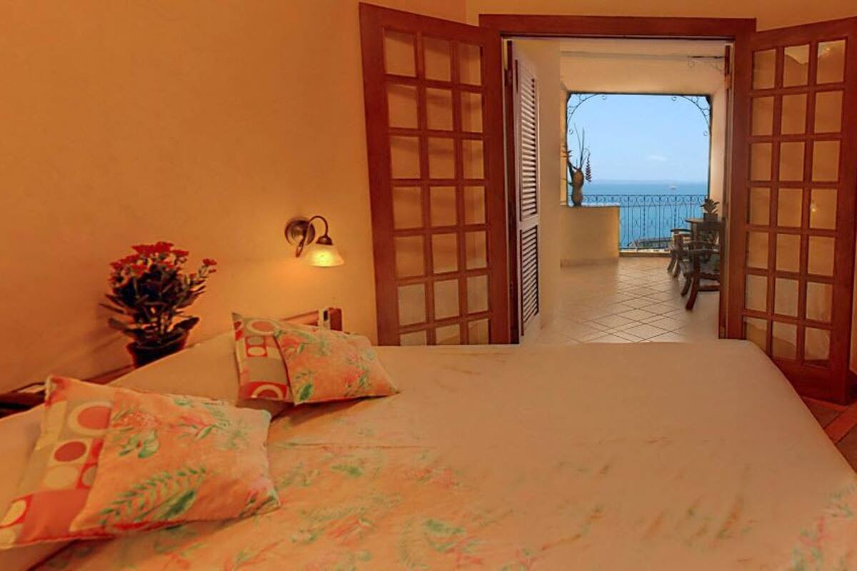A hotel room with an open door leading to a balcony with a view of the sea.
