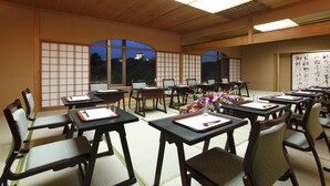 Een traditionele Japanse kamer met tatami vloerbedekking, houten meubels en schuifdeuren. Tafels zijn gedekt met stokjes en een vaas bloemen.
