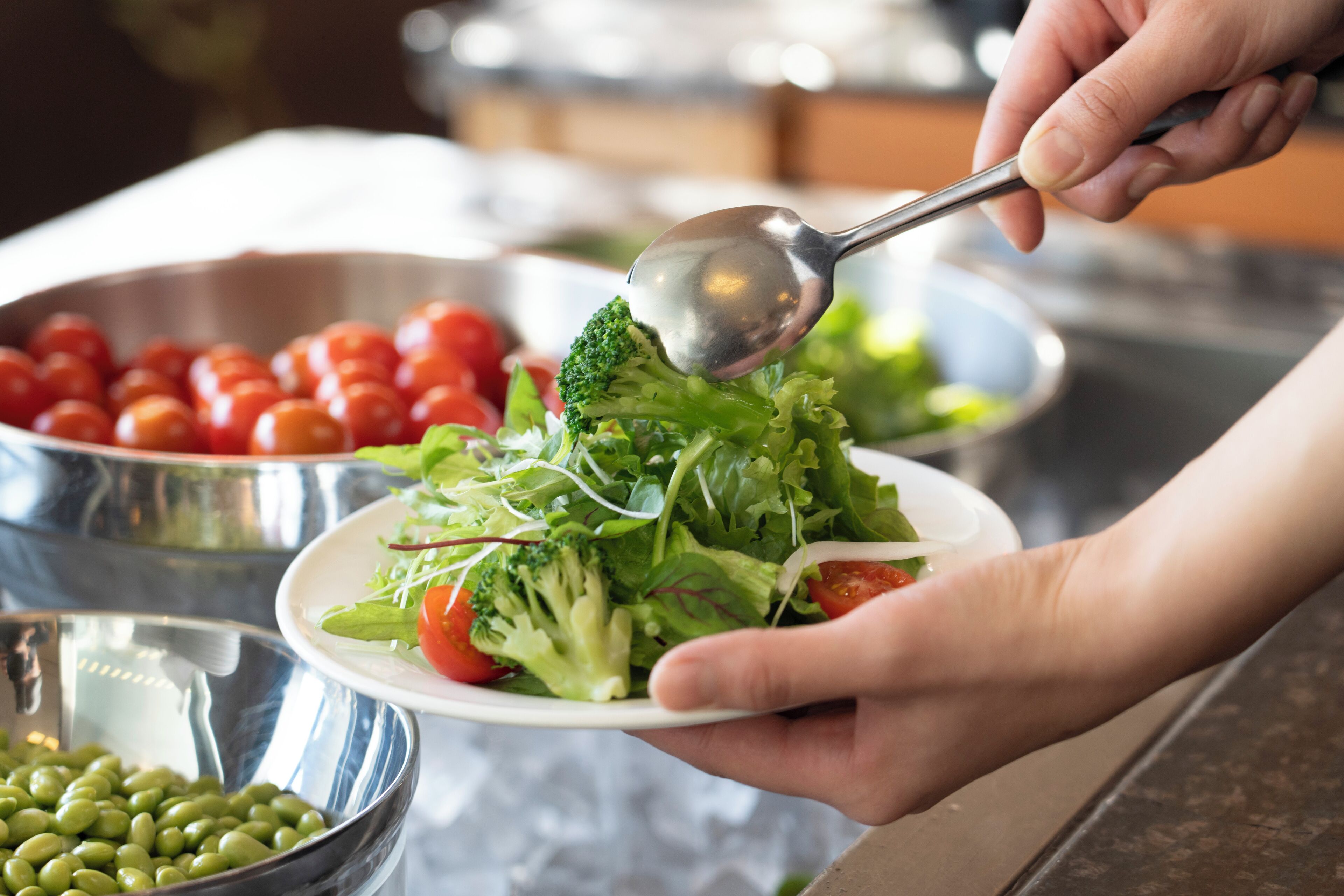 A person holding a plate with a salad, including broccoli and cherry tomatoes, with a spoon.