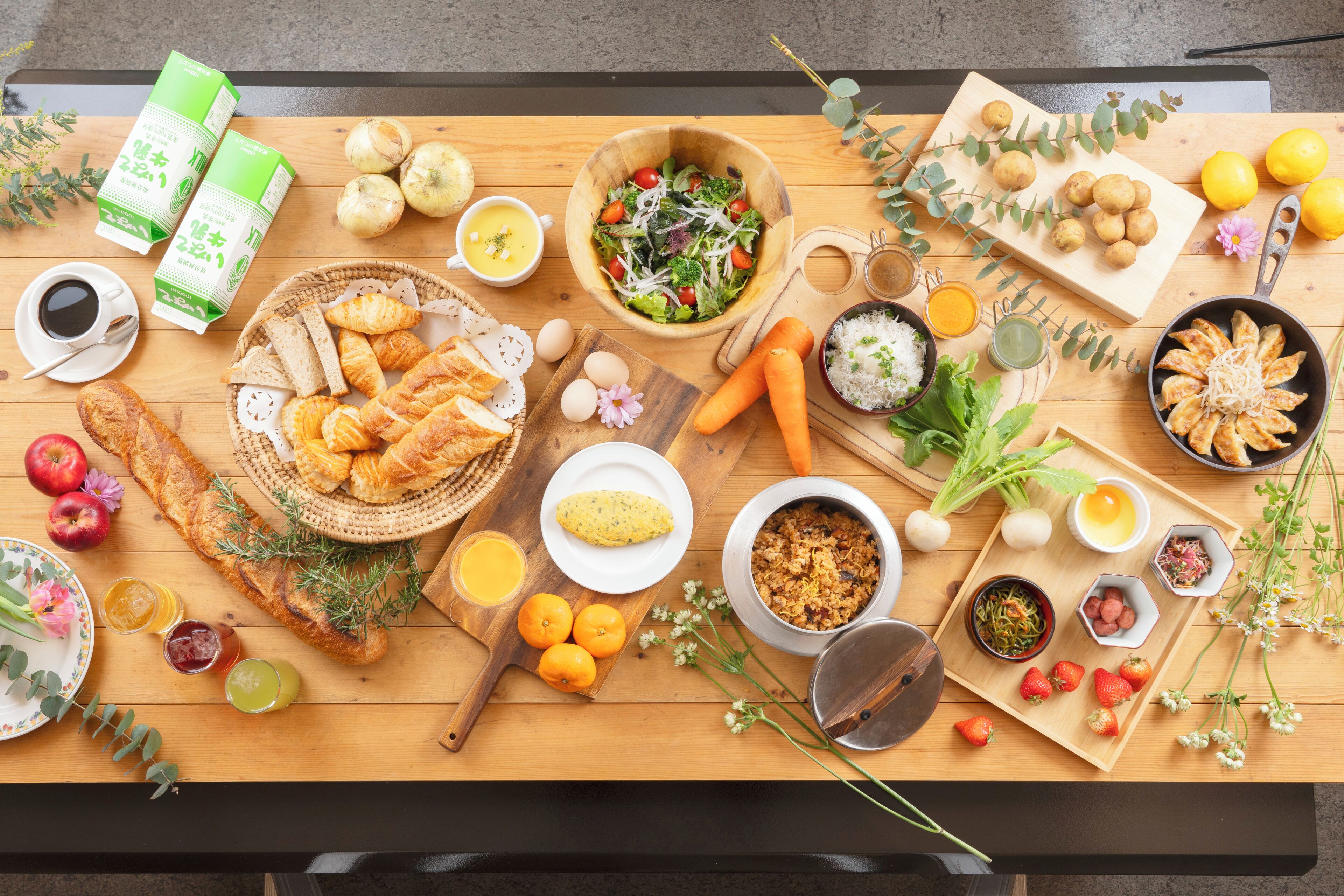 A wooden table with various food items, including bread, fruits, vegetables, and beverages.