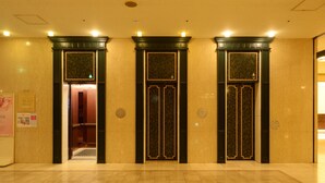 Een hotel lobby met drie liftdeuren, een receptiebalie en een bordje op de muur.