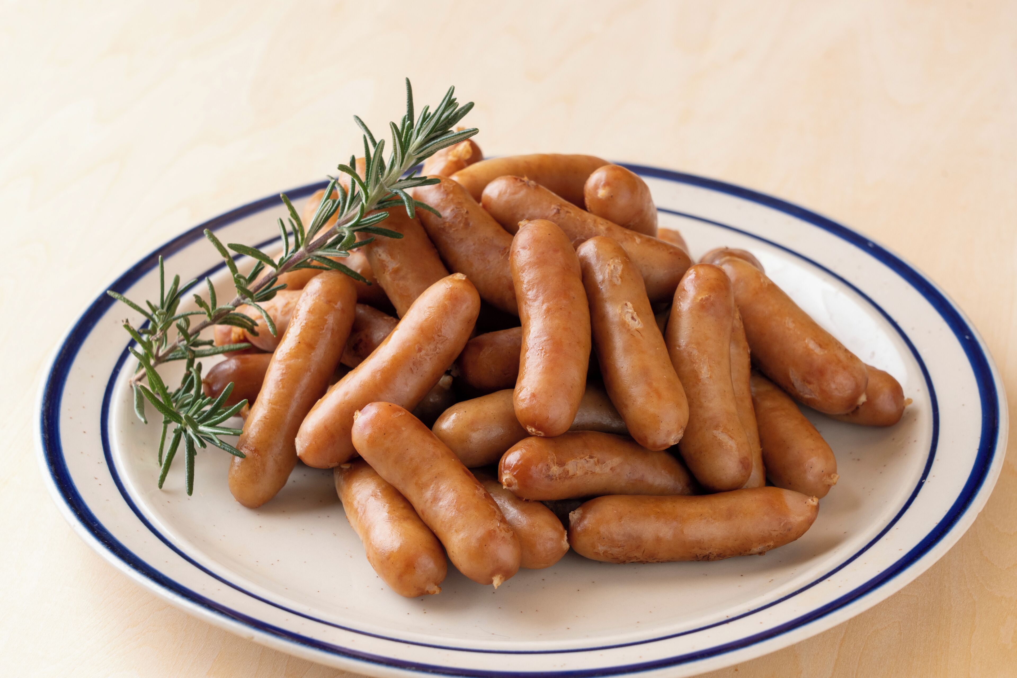 A plate of sausages with rosemary garnish.