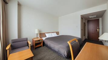 A hotel room with a bed, a desk, a chair, a nightstand, and a door.