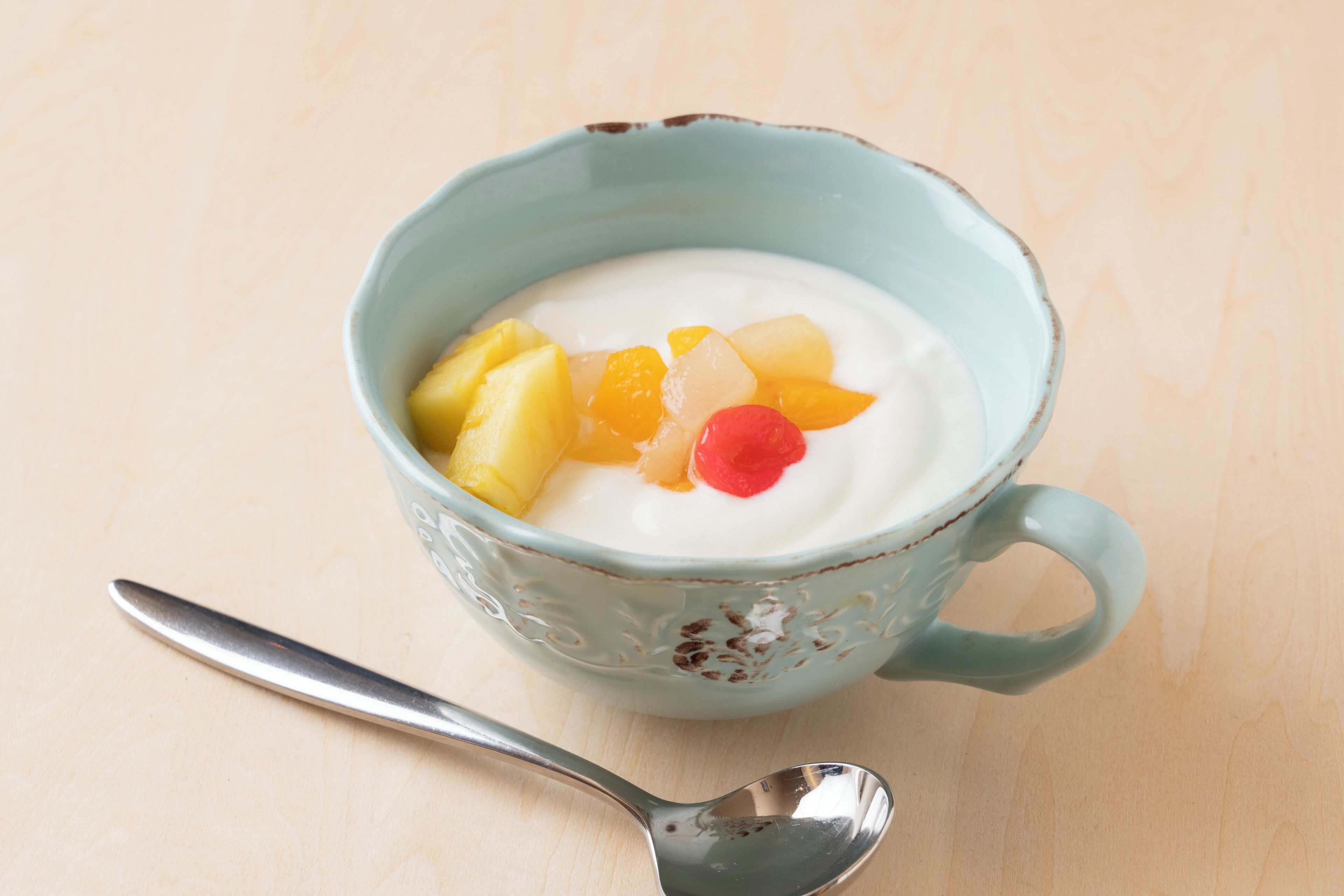 A bowl of yogurt with fruit on a wooden surface.