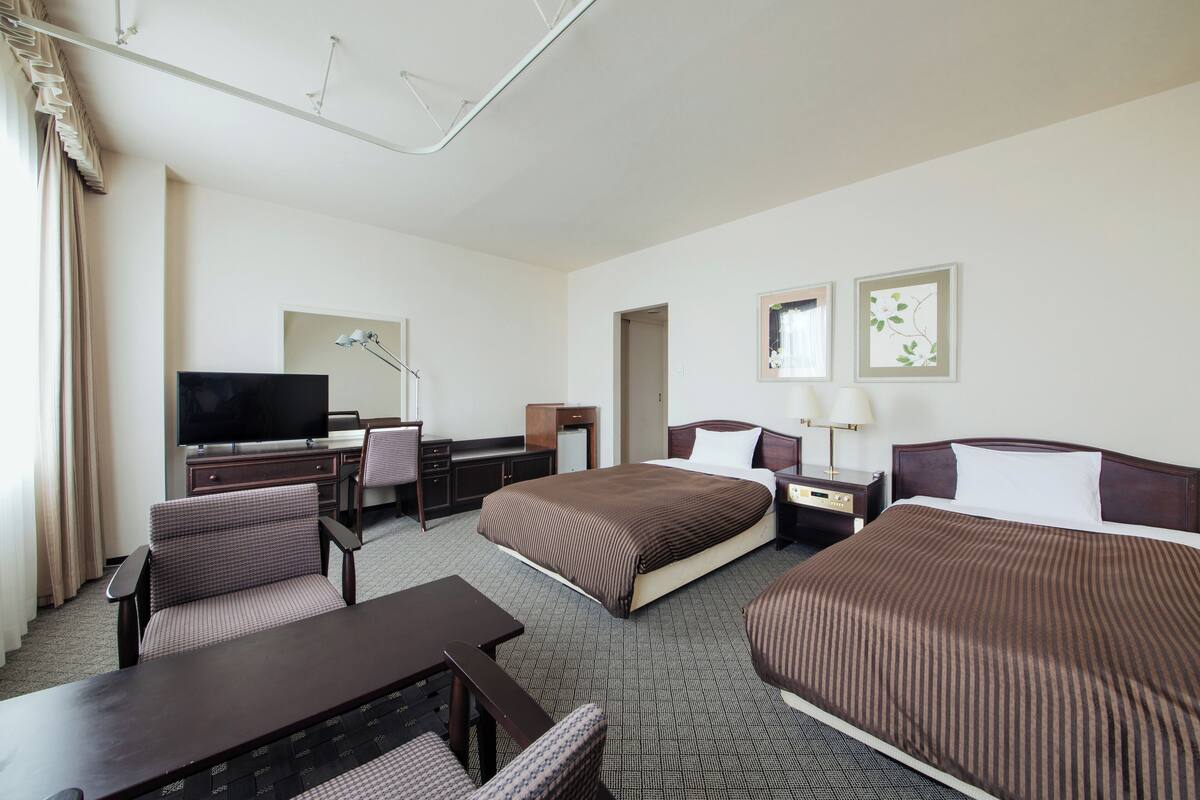 A hotel room with two beds, a desk with a chair, a television, and a lamp.
