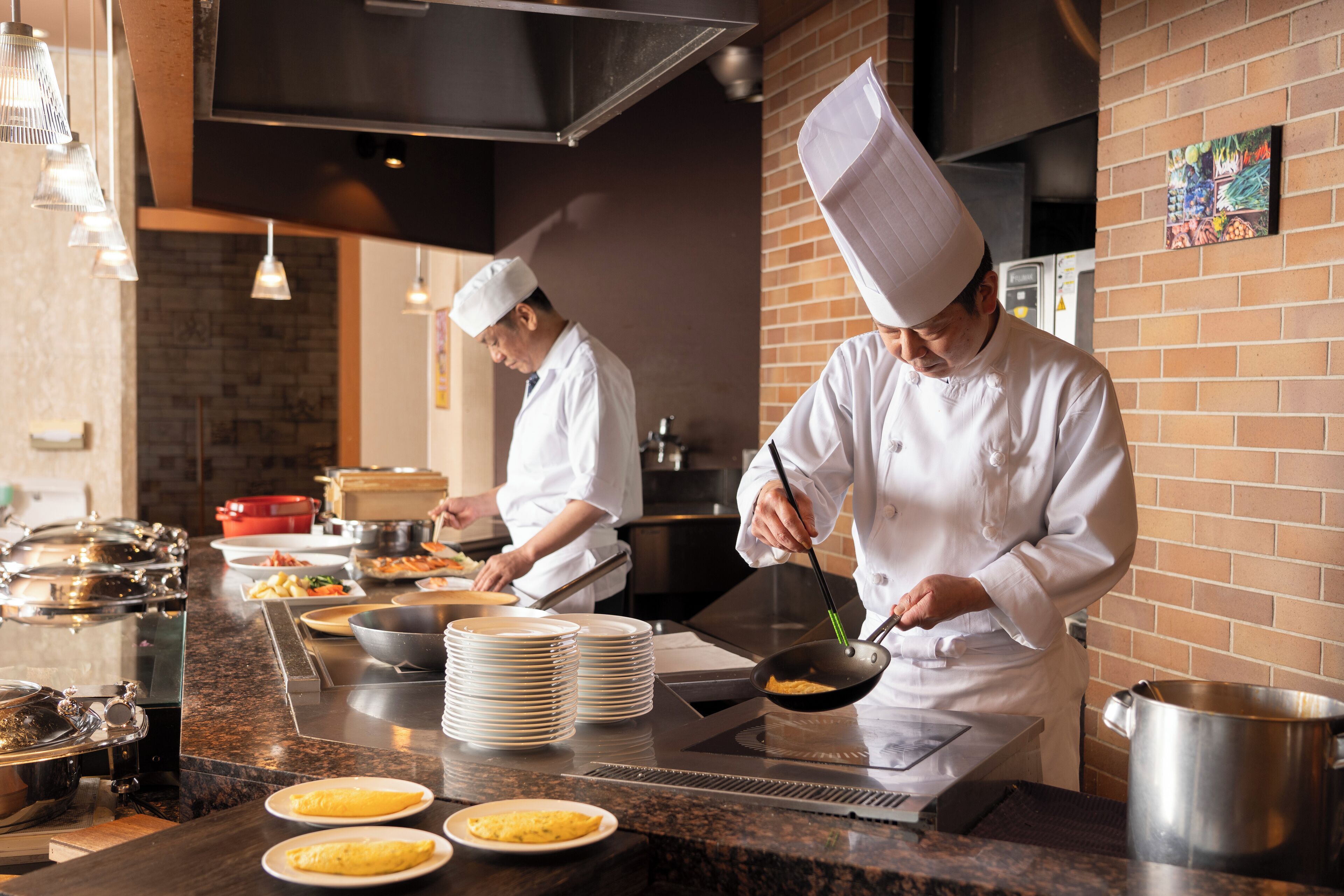 Cocina profesional con chefs preparando alimentos, utensilios de acero inoxidable y pared de ladrillo.