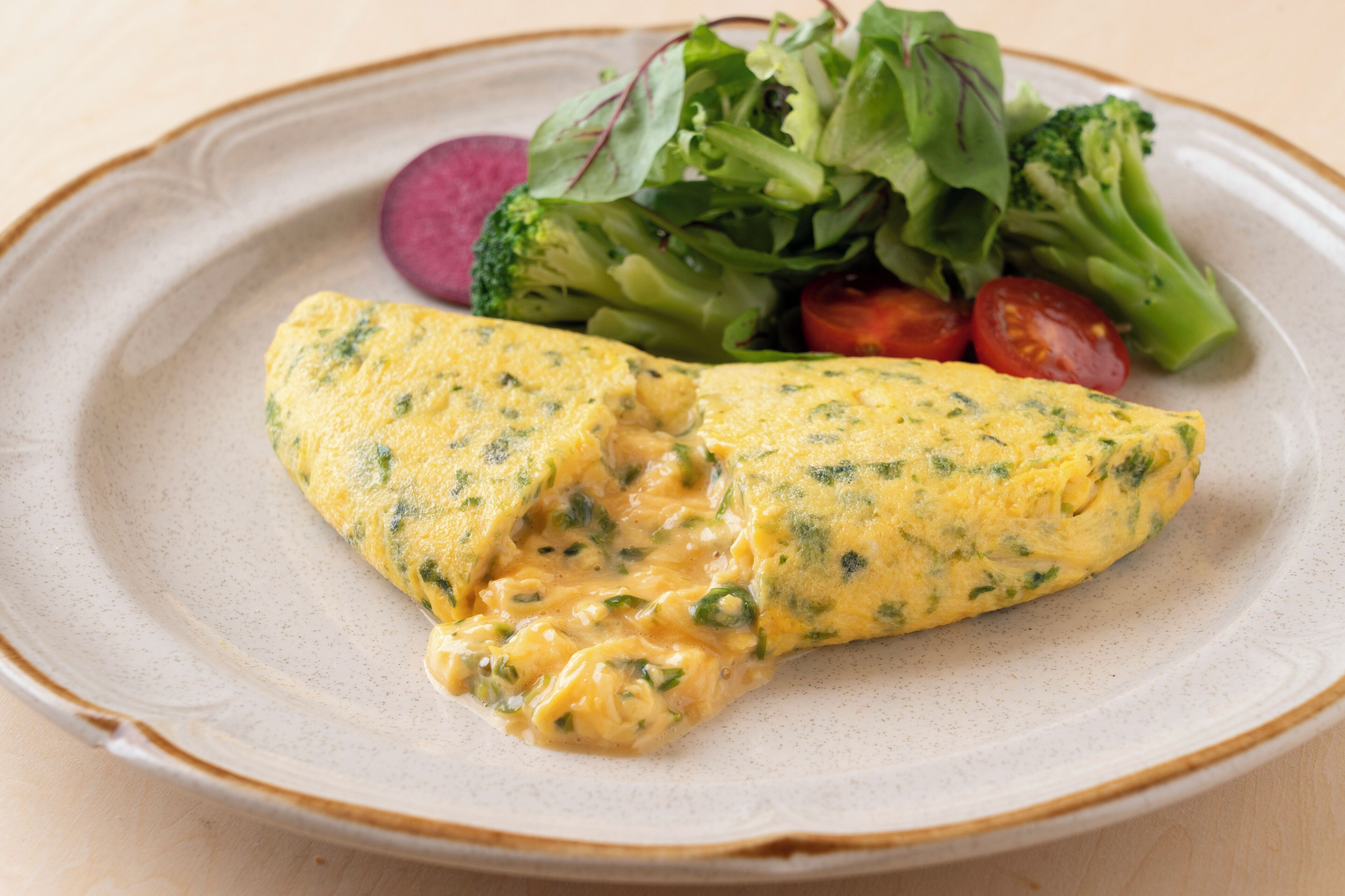 A plate with an omelette, broccoli, and cherry tomatoes.