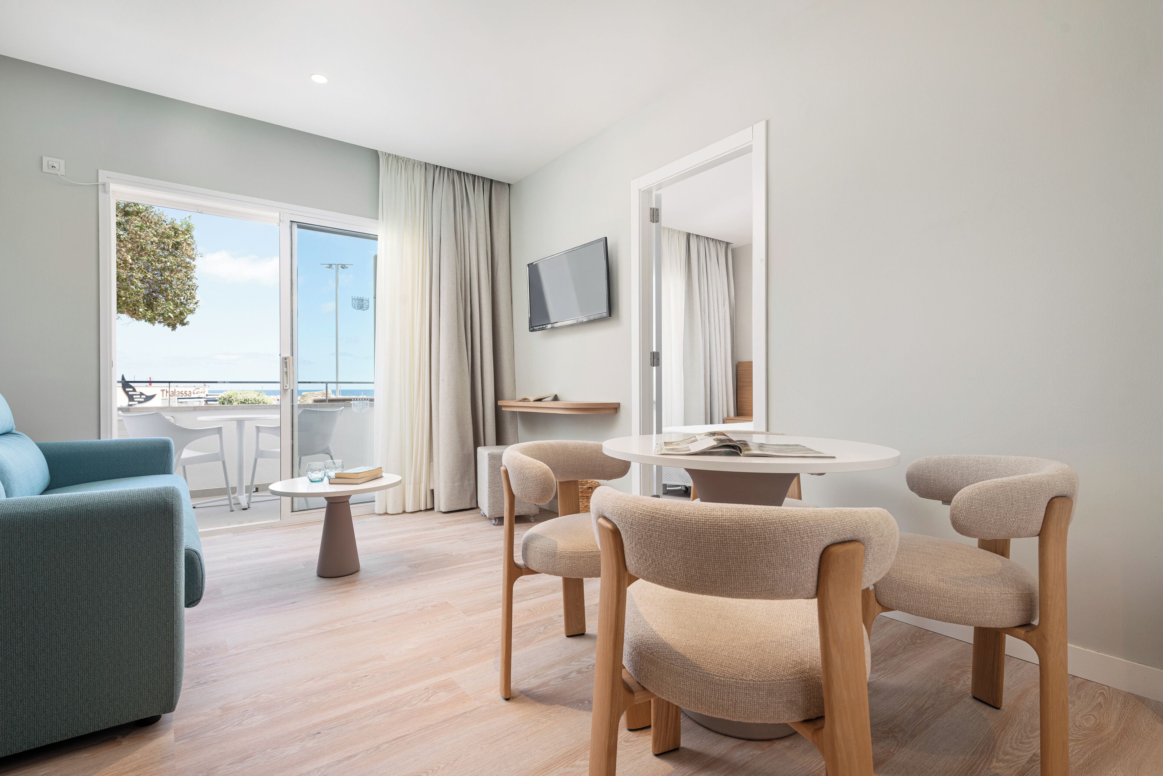 Une chambre d’hôtel moderne dotée d’un balcon, d’une table à manger ronde et d’un téléviseur fixé au mur.
