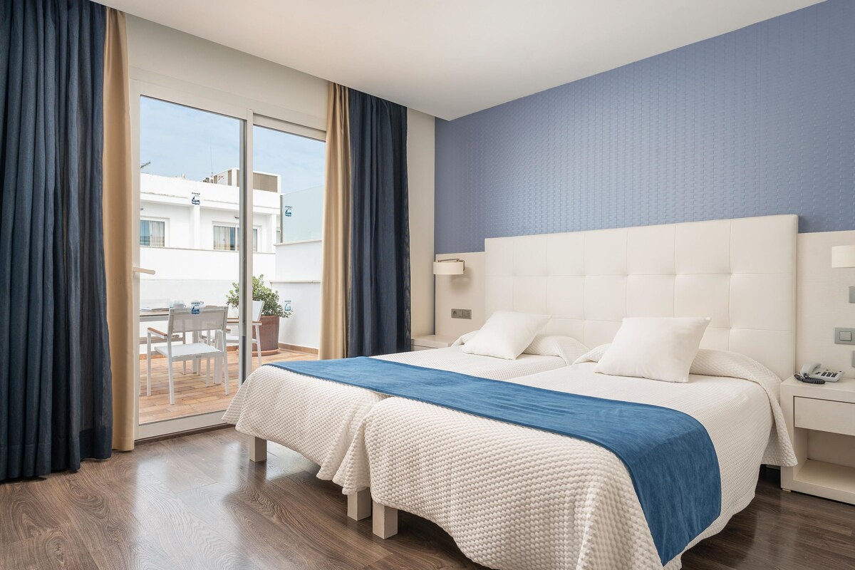 A hotel room with a large bed, a bedside table, a nightstand, and a view of the outside balcony.