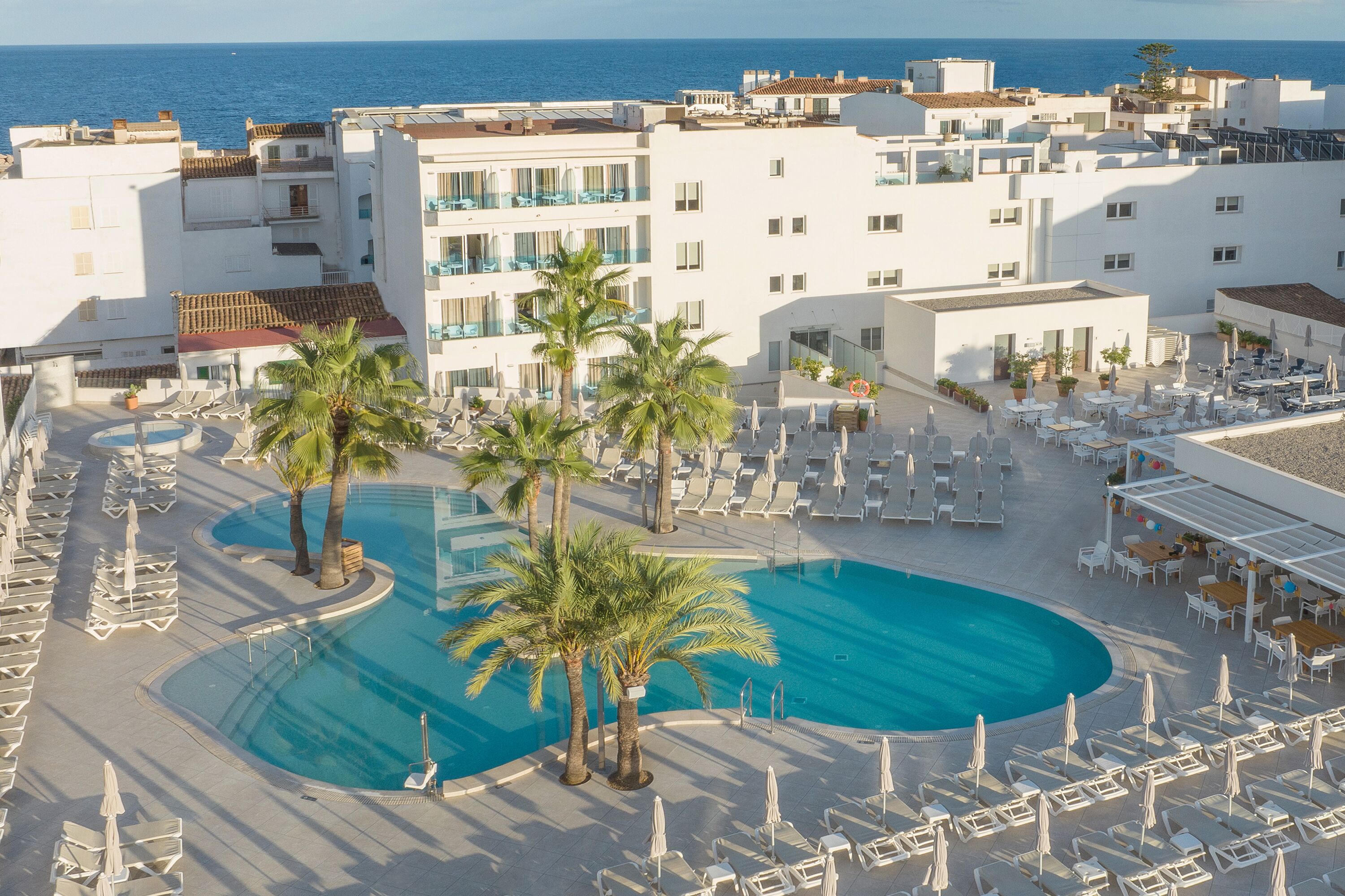 Un resort con una gran piscina, palmeras y vistas al mar.