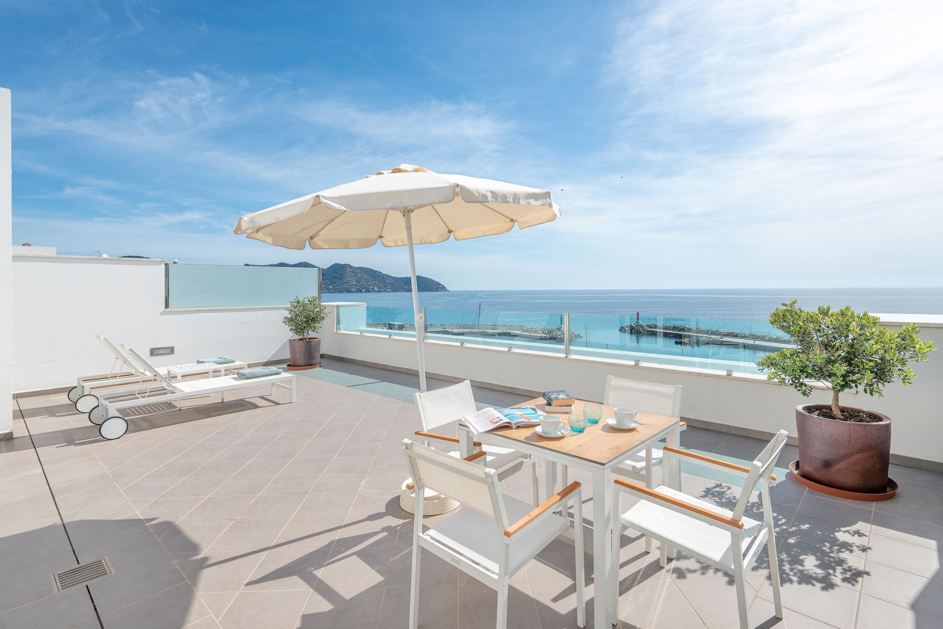 A terrace with a table, chairs, a sun umbrella, lounge chairs, and a potted plant.