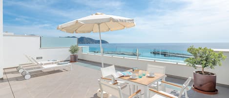 A terrace with a table, chairs, a sun umbrella, lounge chairs, and a potted plant.