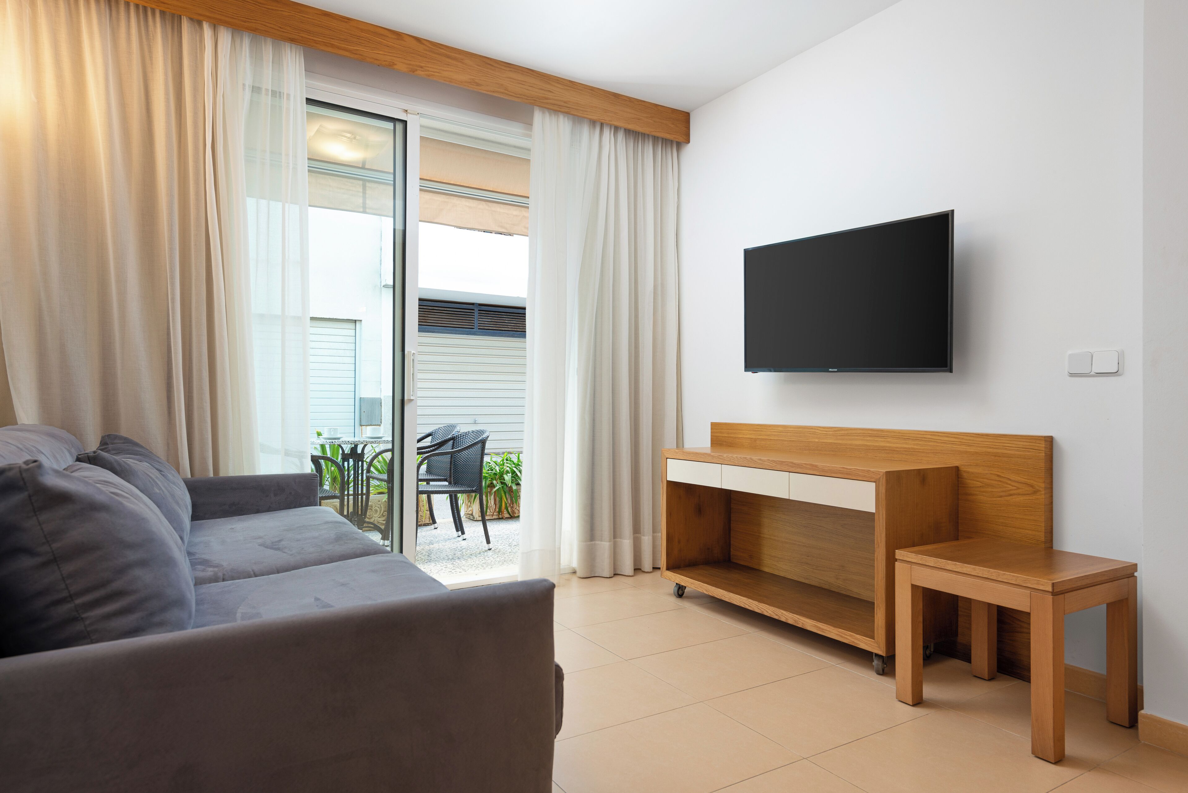 A modern living room with a grey sofa, a wooden console table, and a flat-screen TV mounted on the wall.