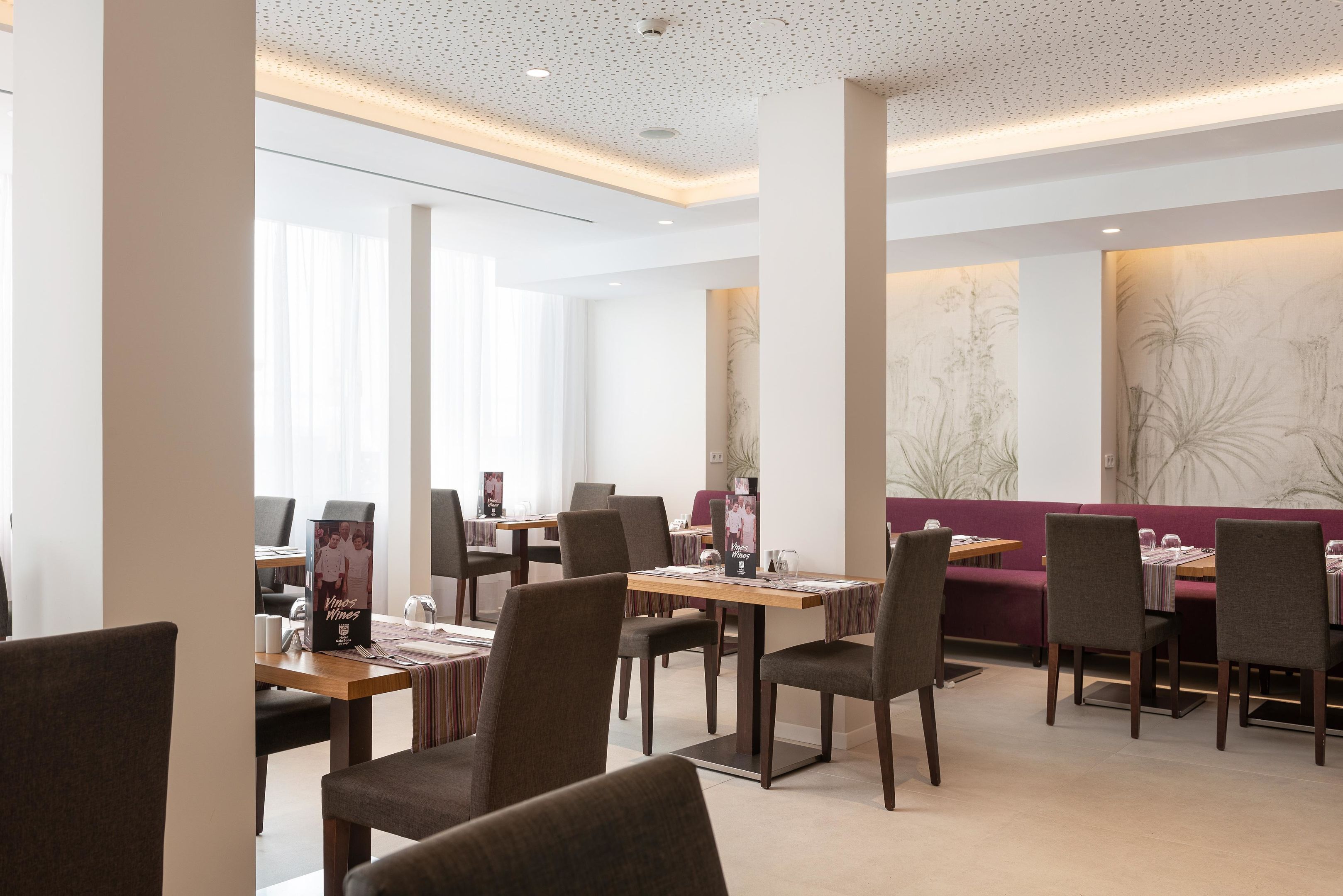 Un espace repas moderne avec des tables et des chaises hautes, de grandes fenêtres et un mur décoratif.