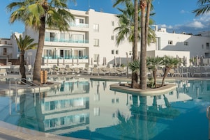 A pool area with lounge chairs, palm trees, and a modern building with balconies.
