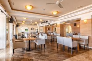 A spacious indoor area with multiple seating arrangements, including tables and chairs, and a ceiling fan.