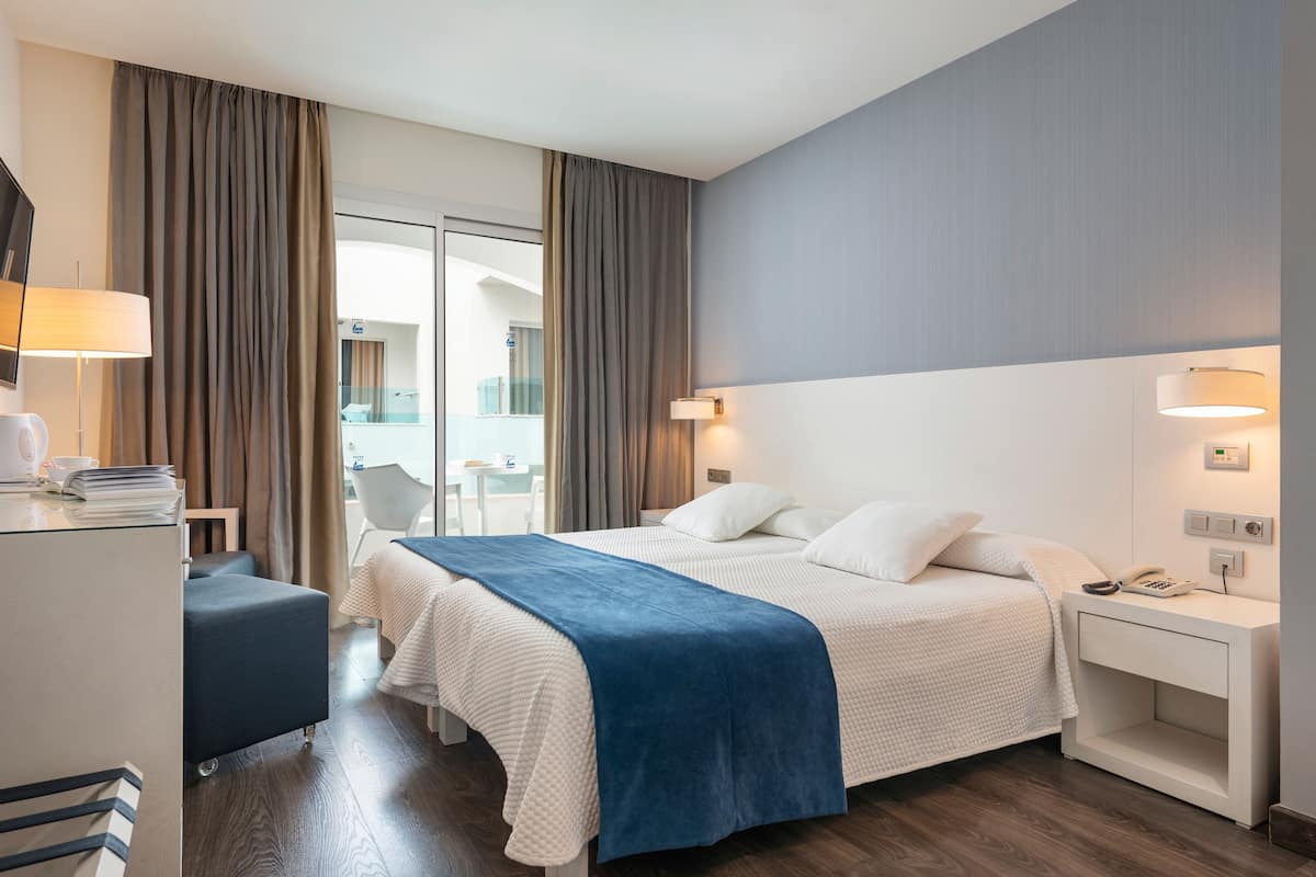 A hotel room with a bed, bedside table, lamp, and a desk with a chair.