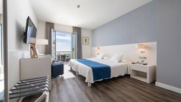 A modern hotel room with a large bed, a desk with a lamp, a TV, and a balcony view.