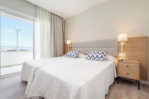 A hotel room with a large bed, two bedside tables, a nightstand, a view of the sea, and a modern design.