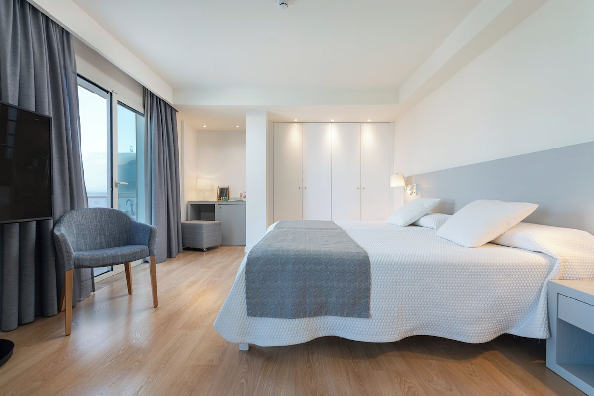 A modern hotel room with a large bed, a chair, a desk, and a TV.
