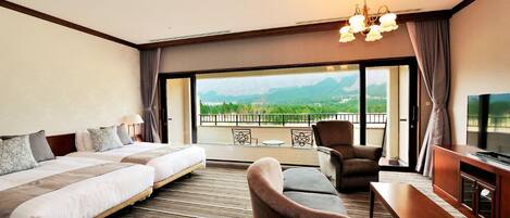 A hotel room with two beds, a sofa, a TV, and a balcony with a mountain view.