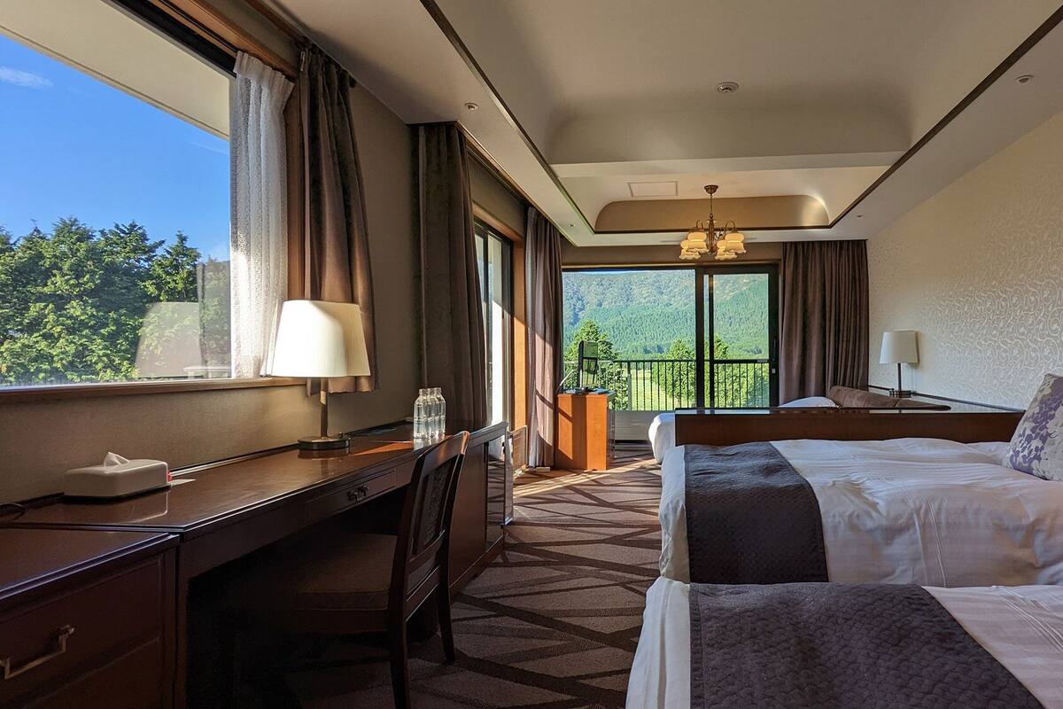 Una camera d'albergo con una scrivania, due letti, vista sul verde e un balcone.