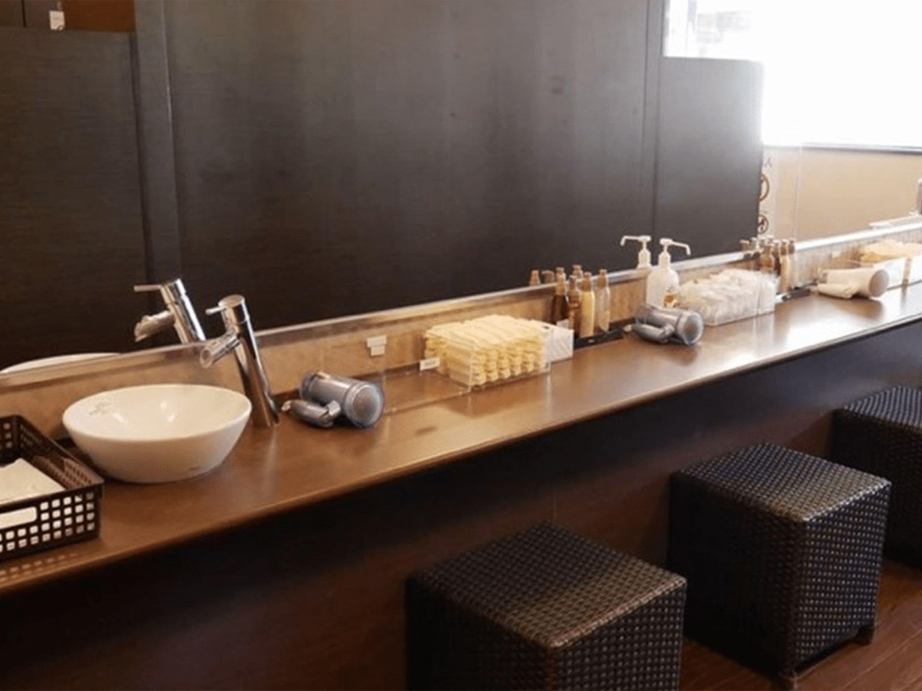 Une salle de bain avec un grand miroir, un lavabo et des articles de toilette posés sur le comptoir. On y trouve des tabourets en osier et un petit panier.