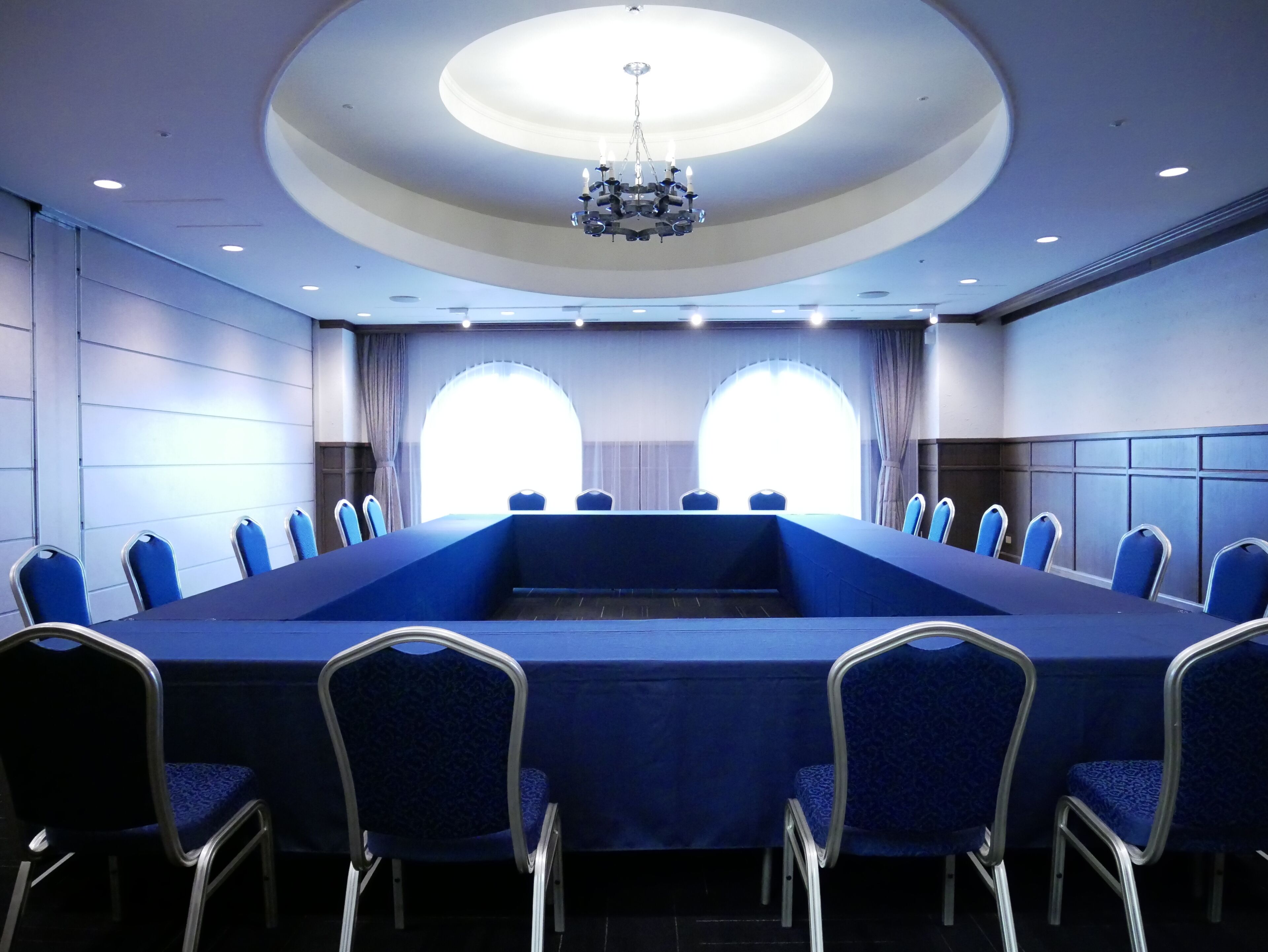 A conference room with a long table, blue chairs, a chandelier, and large windows.
