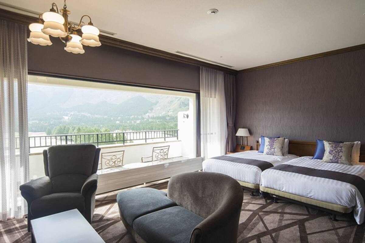 Una camera d'albergo con due letti, un divano, un tavolino e un balcone vista montagna.
