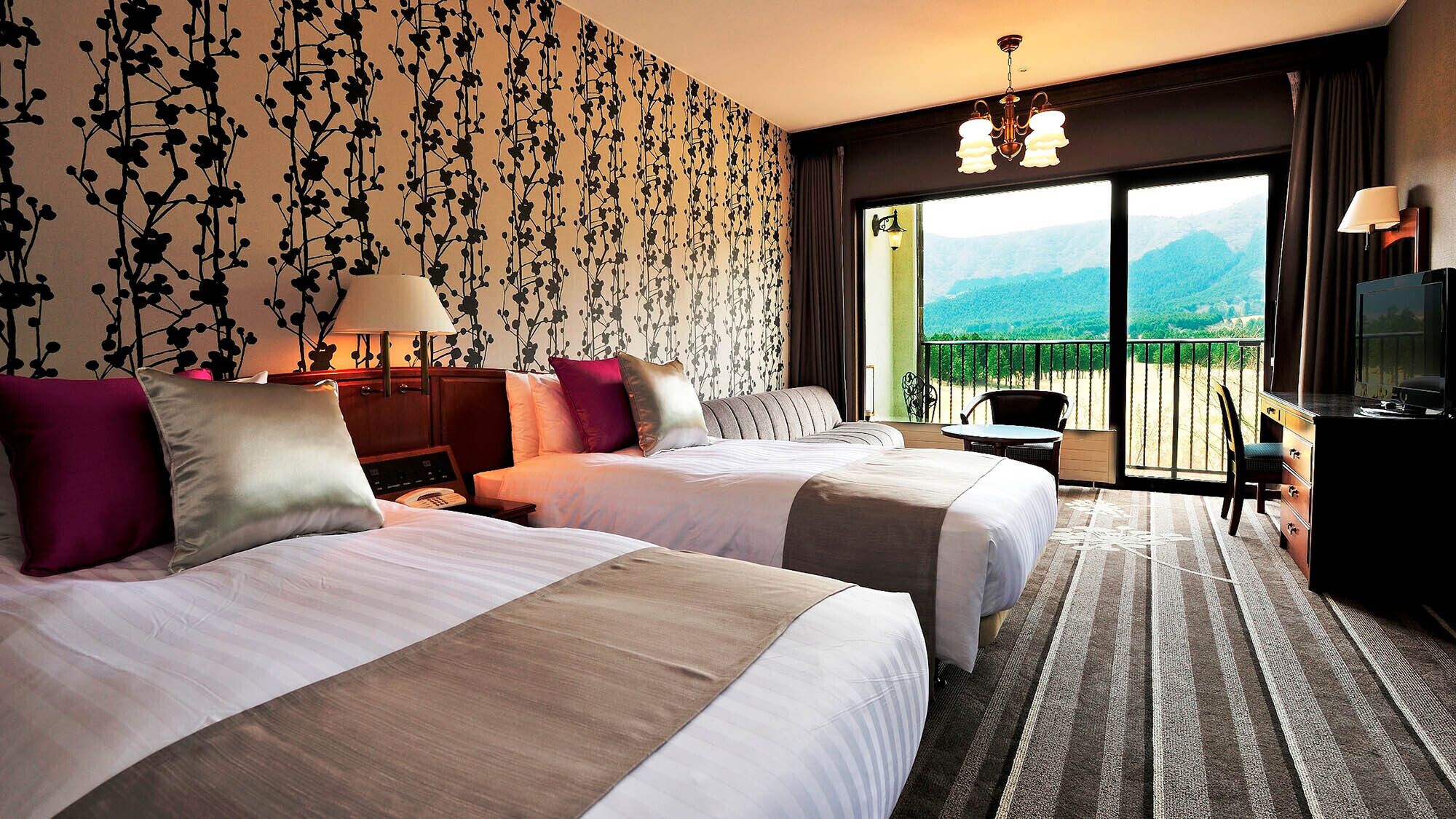 A hotel room with two beds, a desk, a chair, and a balcony with a mountain view.