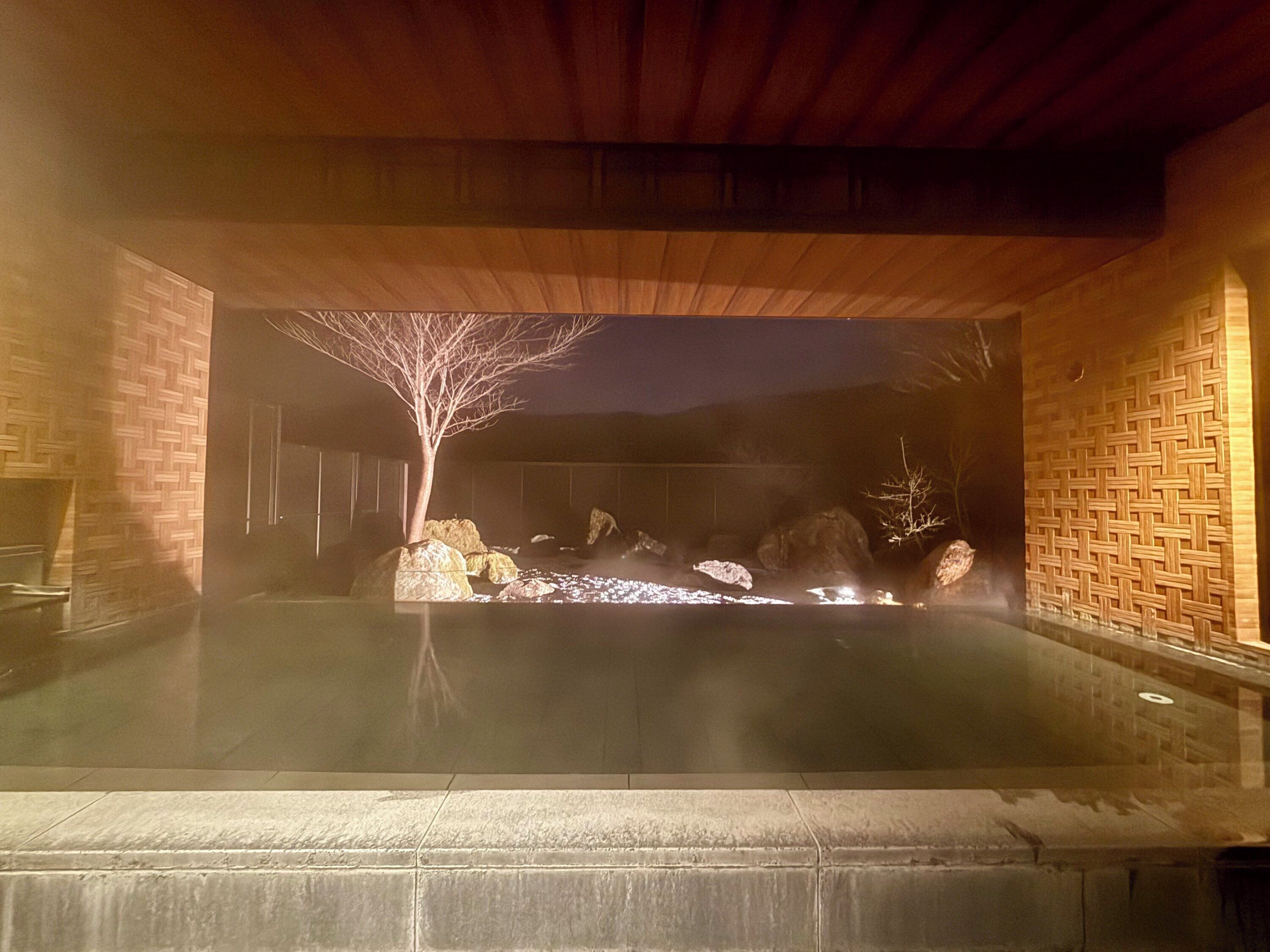 A hot tub area with a wooden ceiling, stone walls, and a tree in the center.
