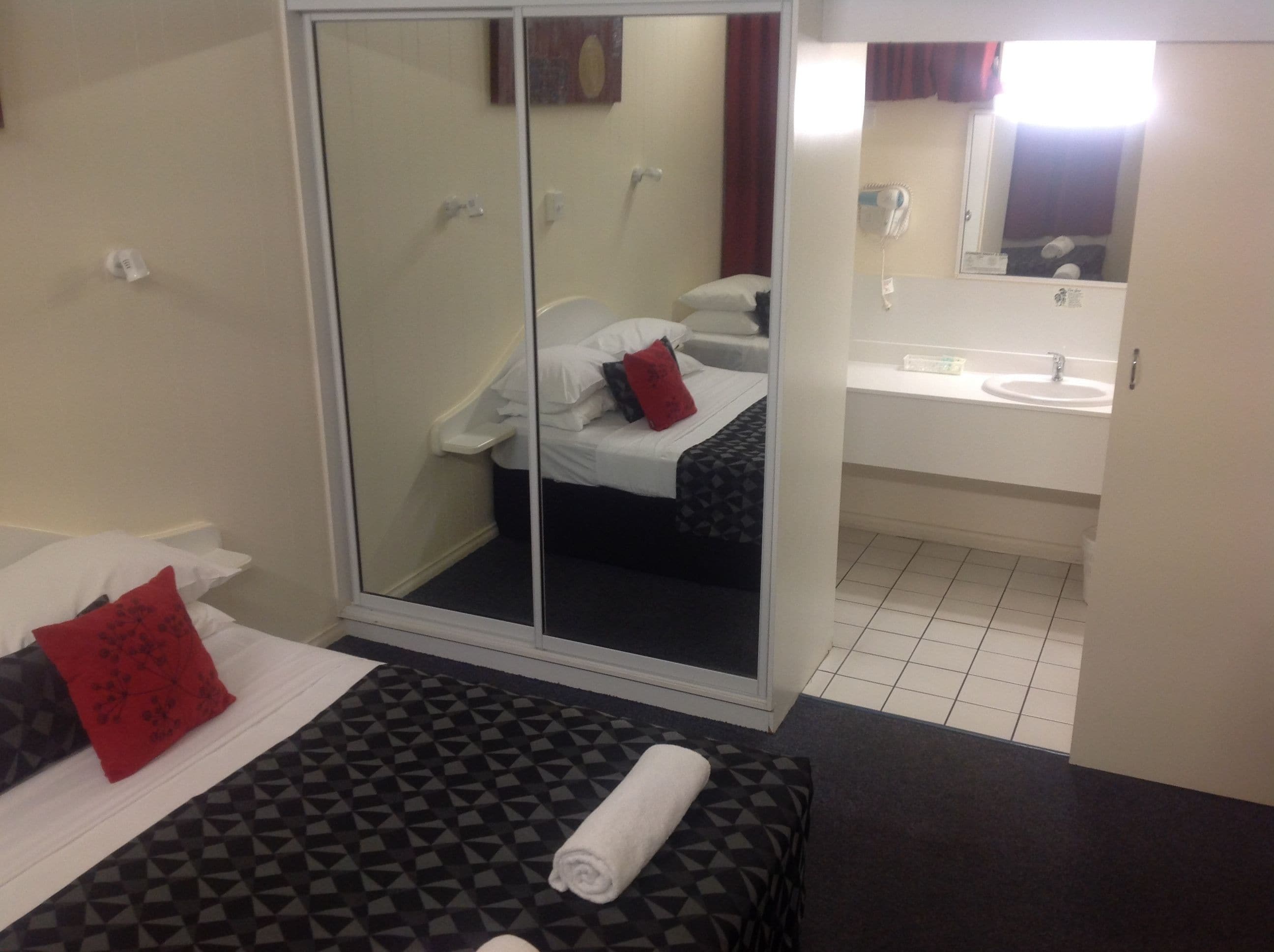 Ein Hotelzimmer mit Bett, einem Badezimmer mit Waschbecken und Spiegel sowie einer Schiebetür zu einem Duschbereich.
