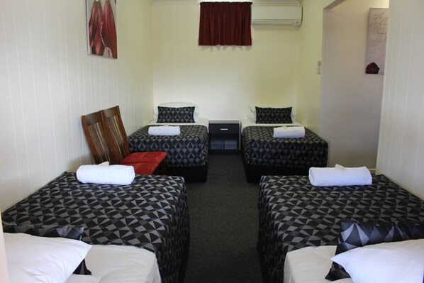 A room with two beds, each with patterned bedding and white pillows. There is a wooden chair and a small table between the beds.