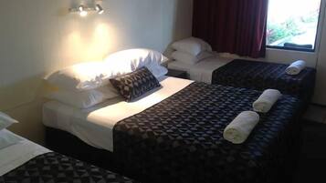 A hotel room with two single beds, a large bed with a patterned bedspread, and a window with curtains.