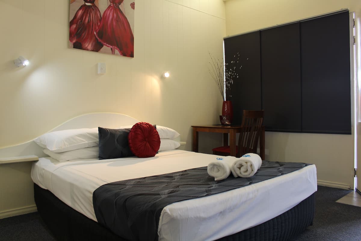 Ein Hotelzimmer mit Bett, Schreibtisch, Stuhl, einem Bild an der Wand und einem Fenster.