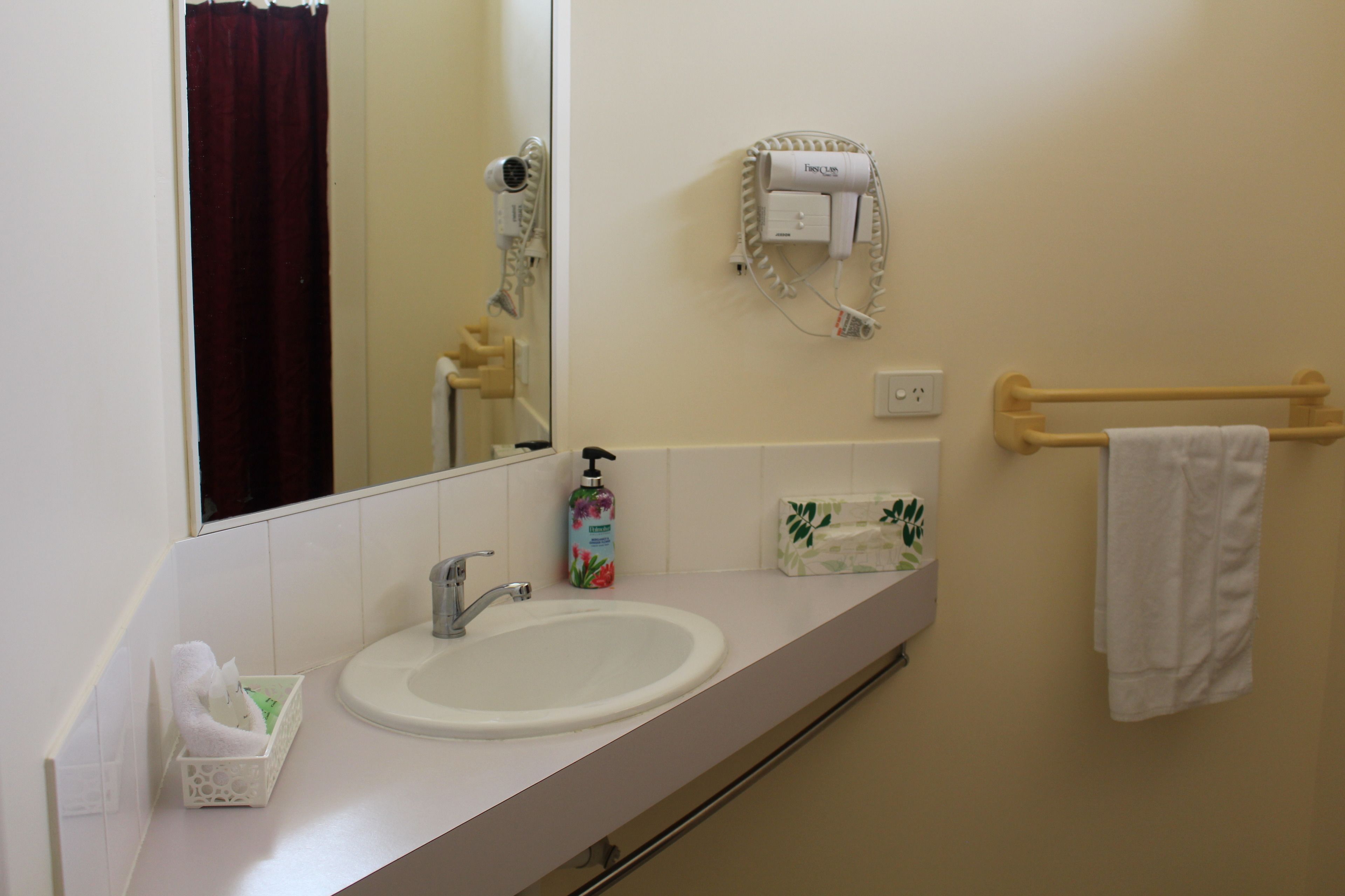 Ein Badezimmer mit Waschbecken, Spiegel, Fön und Handtuchhalter.