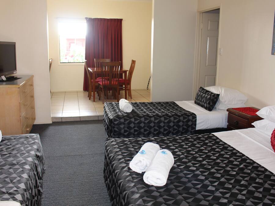 A hotel room with two beds, a TV on a dresser, and a dining area with a table and chairs.